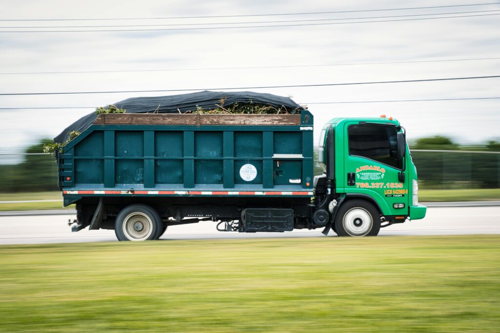 pexels-photo-11521609-11521609 A green truck transporting yard waste on a road captured in motion. Perfect for transportation and environmental themes.