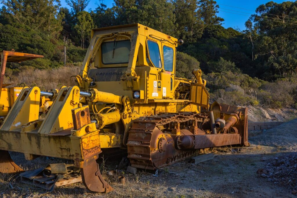 pexels-photo-14484393 A yellow bulldozer with rust stands outdoors surrounded by nature.